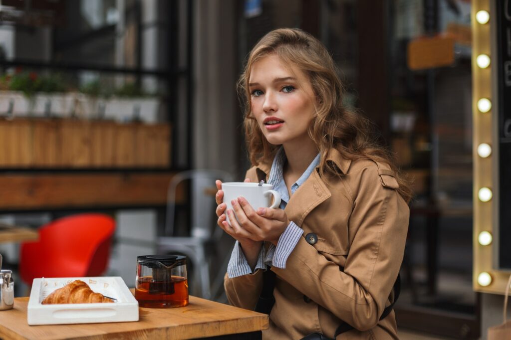 Young attractive woman in trench coat dreamily looking in camera
